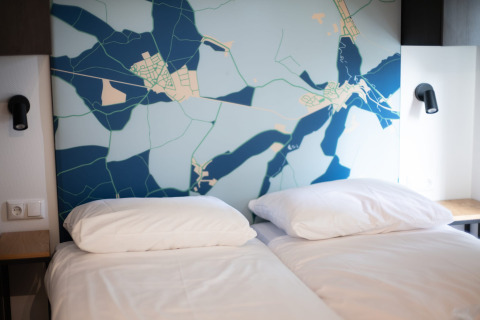 Chambre moderne avec deux lits simples, linge blanc et tête de lit décorée d'une carte au Resort Gulpen 7.