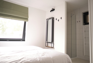 Lichte slaapkamer met groot raam, bed en moderne ensuite badkamer in Resort Gulpen 7, Nederland.
