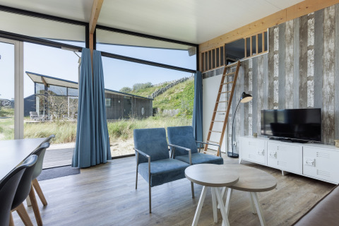 Moderne woonkamer in Sea Lodges Bloemendaal 5, Nederland met grote ramen, blauwe zetels en mezzanine.
