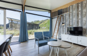 Salon moderne dans Sea Lodges Bloemendaal 5 aux Pays-Bas avec grandes fenêtres, fauteuils bleus et mezzanine.