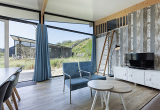 Moderne woonkamer in Sea Lodges Bloemendaal 5, Nederland met grote ramen, blauwe zetels en mezzanine.