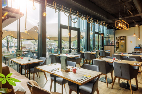 Licht, modern restaurant in een glampinglocatie met grote ramen en gezellig buitenterras.