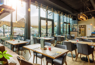 Licht, modern restaurant in een glampinglocatie met grote ramen en gezellig buitenterras.