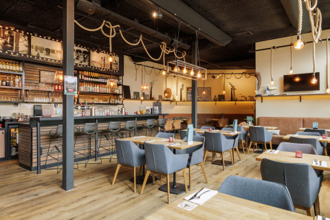 Modern restaurant in een glamping met comfortabele zitplaatsen, houten tafels en touwdecoratie boven.