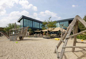 Aire de jeux extérieure avec structures en bois devant un hébergement glamping moderne en verre.