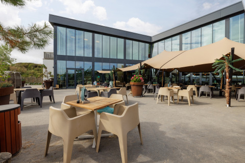 Buiten eetruimte aan glamping-accommodatie met modern glazen gebouw en ruime schaduwzeilen.