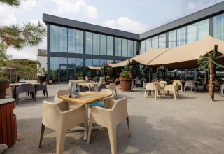 Buiten eetruimte aan glamping-accommodatie met modern glazen gebouw en ruime schaduwzeilen.