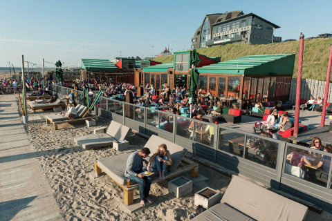 Bezoekers genieten van het zonnige weer op loungebanken aan een strand glamping accommodatie aan zee.