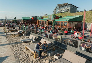 Bezoekers genieten van het zonnige weer op loungebanken aan een strand glamping accommodatie aan zee.
