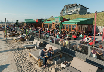 Des personnes détendues sur des transats et canapés à un hébergement glamping en bord de plage, au soleil.