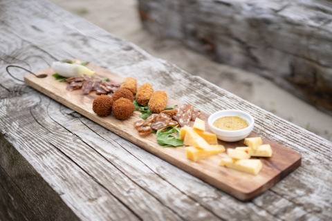 Houten plank met kaas, salami, kroketjes en dipsaus buiten bij een glamping verblijf.