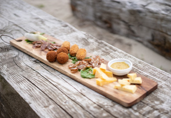 Planche en bois avec fromages, charcuterie, croquettes et sauce à l’extérieur dans un glamping.