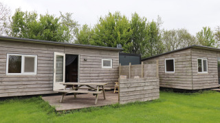Chalet Cosy cabin 1 avec façade en bois, terrasse, table de pique-nique et pelouse verte arborée.