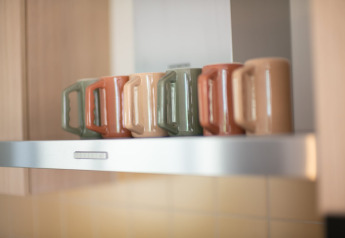 Fem kaffekrus i forskellige farver står på en hylde i køkkenet på Resort «Gulpen 7» i Holland.