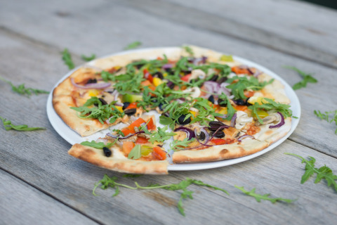 Vegetarische pizza met rucola en kleurrijke groentjes op een bord tijdens een glampingverblijf.