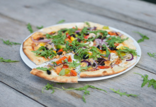 Vegetarische pizza met rucola en kleurrijke groentjes op een bord tijdens een glampingverblijf.