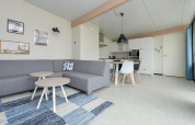 Modernes Wohnzimmer und KĂĽche im Sea Lodges Bloemendaal 4 Strandhaus in den Niederlanden, graues Sofa.