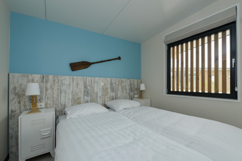Slaapkamer in Sea Lodges Bloemendaal 4 in Nederland met twee bedden, blauwe wand en ruim venster.