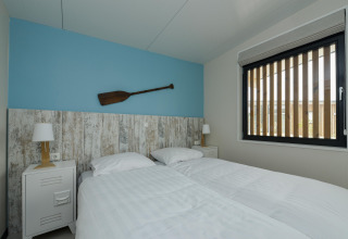 Slaapkamer in Sea Lodges Bloemendaal 4 in Nederland met twee bedden, blauwe wand en ruim venster.