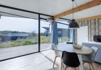 Helles Wohnzimmer in Sea Lodges «Bloemendaal 4» mit Panoramablick auf die Dünenlandschaft in den Niederlanden.