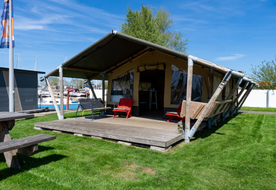 Safari-Zelt Heeg für 4 Personen mit Terrasse, Liegestühlen und Blick auf den Jachthafen im Freien.