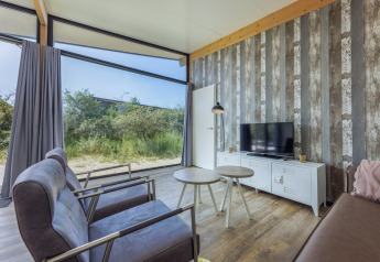 Salon moderne avec grandes fenêtres, vue nature et TV aux Sea Lodges Bloemendaal 3, Pays-Bas.