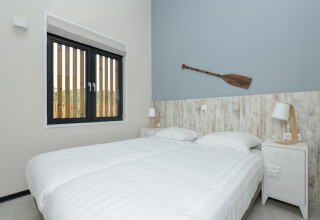Lichte slaapkamer met twee eenpersoonsbedden, raam en een houten peddel aan de muur in Sea Lodges Bloemendaal.