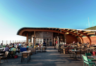 Buitenterras van een lodge met houten tafels, waar gasten genieten onder een stralend blauwe hemel.