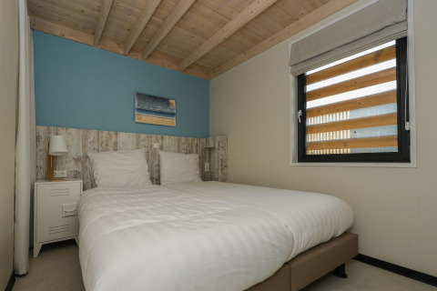 Slaapkamer in strandhuis Sea Lodges Bloemendaal 2 in Nederland met houten plafond en dubbel bed.