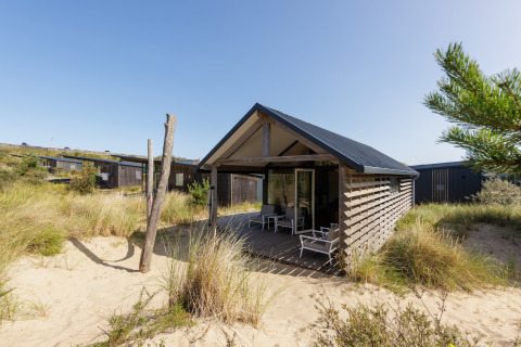 Modern strandhuis bij Sea Lodges Bloemendaal 2, omgeven door zand en duingras onder een heldere lucht.