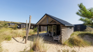 Modern strandhuis bij Sea Lodges Bloemendaal 2, omgeven door zand en duingras onder een heldere lucht.
