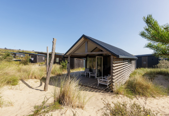 Modern strandhuis bij Sea Lodges Bloemendaal 2, omgeven door zand en duingras onder een heldere lucht.