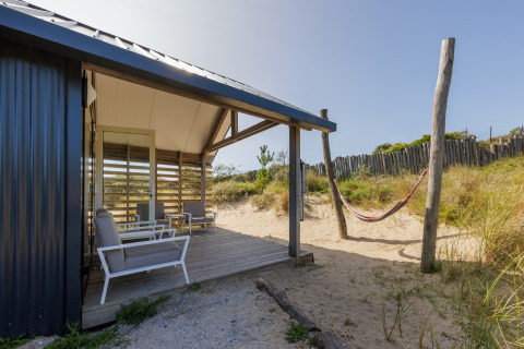 Strandhuis met overdekt terras, stoelen en hangmat in het zand bij Sea Lodges Bloemendaal, Nederland.