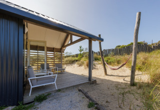 Strandhuis met overdekt terras, stoelen en hangmat in het zand bij Sea Lodges Bloemendaal, Nederland.
