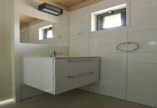 Moderne badkamer met zwevend wit meubel, kleine ramen en wandtegels in Sea Lodges Bloemendaal, NL.
