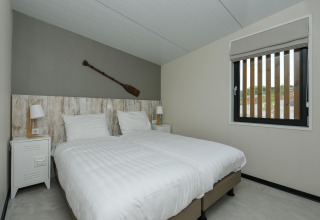 Slaapkamer in Sea Lodges Bloemendaal 1 Nederland met twee eenpersoonsbedden en een peddel aan de wand.
