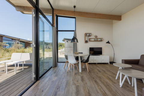 Moderne leefruimte in Sea Lodges «Bloemendaal 1» met grote ramen en zicht op het terras buiten.