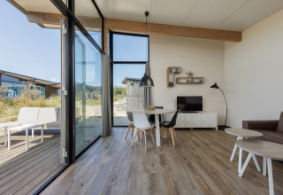 Moderne leefruimte in Sea Lodges «Bloemendaal 1» met grote ramen en zicht op het terras buiten.