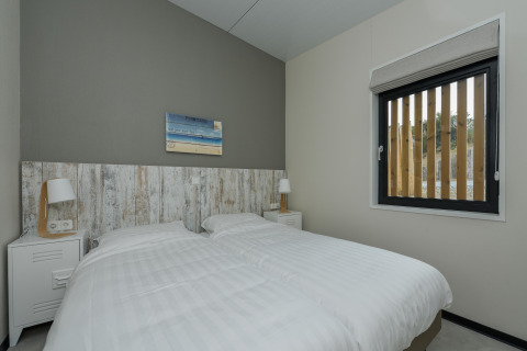 Moderne slaapkamer met twee eenpersoonsbedden, nachtkastjes en lampen in Sea Lodges Bloemendaal 1, Nederland.