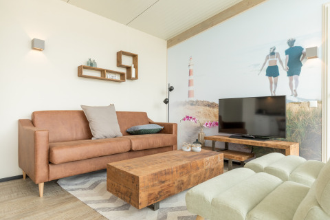 Woonkamer in Sea Lodges Ameland 3 met bruine zetel, houten tafel, tv en strandmuurdecoratie.