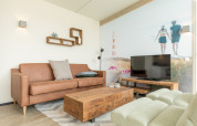 Modernes Wohnzimmer in Sea Lodges Ameland 3 mit Ledersofa, Holztisch, TV und Wandbild am Strand.