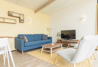 Lichte moderne woonkamer in Sea Lodges Ameland 2 met blauwe zetel, tv en gele accenten in Nederland.