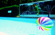 Un ballon de plage coloré flotte dans la piscine d’un lodge, avec jets d’eau colorés en arrière-plan.