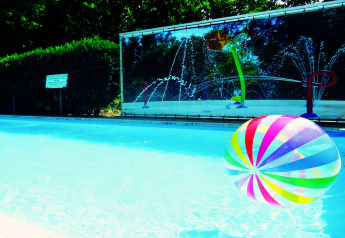 A colorful beach ball floats in a bright outdoor lodge pool, with playful water features in the background.