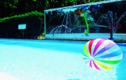 Un colorido balón de playa flota en la piscina de un lodge, con divertidos chorros de agua al fondo.