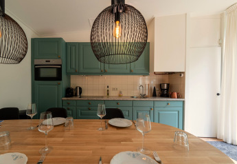 Modernes Küche und Essbereich mit grünen Schränken, Holztisch und Designerlampen in der Wellnes suite.