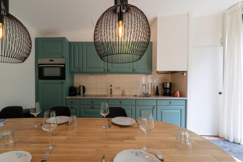 Moderne køkken og spiseplads med grønne skabe, trægulv og elegante hængende lamper i Wellnes suite.