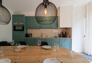 Moderne køkken og spiseplads med grønne skabe, trægulv og elegante hængende lamper i Wellnes suite.