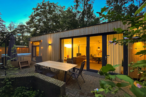 Udendørs område ved Wellnes suite-lodge med terrasse, bord, stole og oplyst opholdsstue om aftenen.