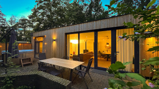 Outdoor area of Wellnes suite lodge with patio, table, chairs, and warmly lit living room during evening.